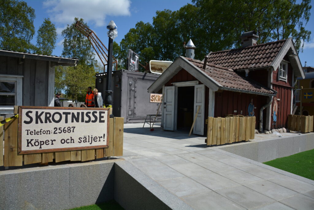 Lekplats med små byggnader och handmålad skylt "SKROTNISSE"