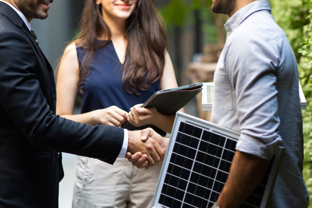 Tre personer står i lummig miljö. En håller i solceller. Två skakar hand.