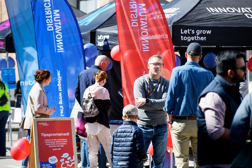 Personer står och pratar framför eventtält och beachflaggor