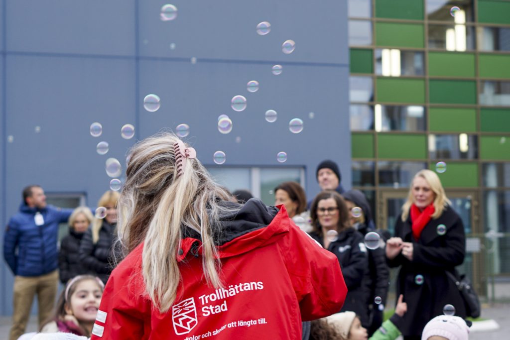 En kvinna från Trollhättan stad och barn som leker med såpbubblor. Det är vuxna i bakgrunden