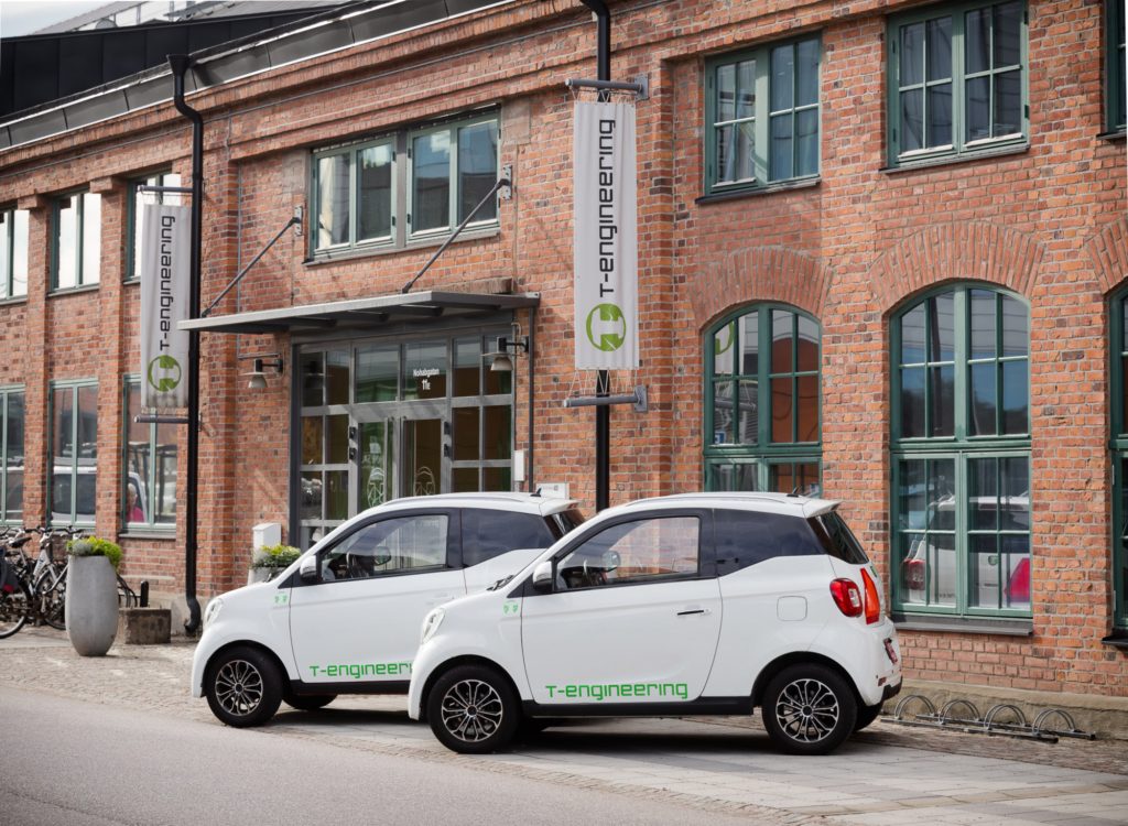 Två vita bilar med T-engineering logga framför T-engineering fasad.