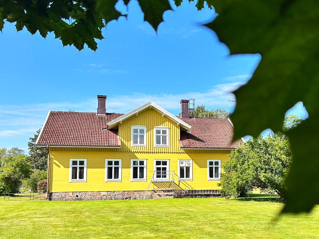Ett gul hus på gården med massa träd runt om det