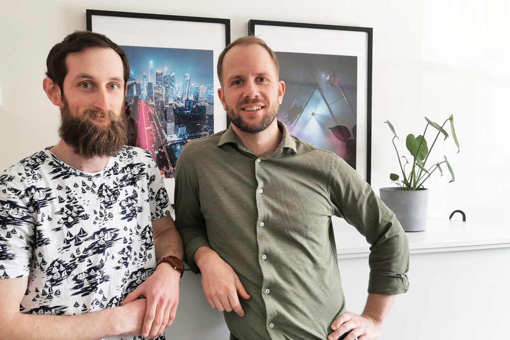 Patrik Birgersson och Marcus Munther står tillsammans framför en hylla dekorerad med tavlor och krukväxt