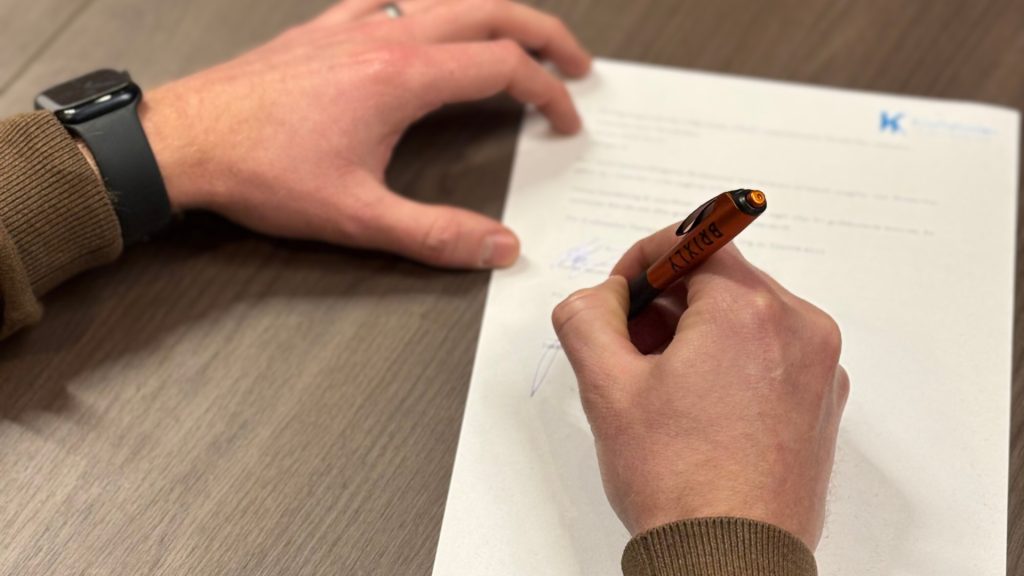 Två händer, en av de håller avtalet och den andra en penna med märket BRIXL som används för att signera avtalet.