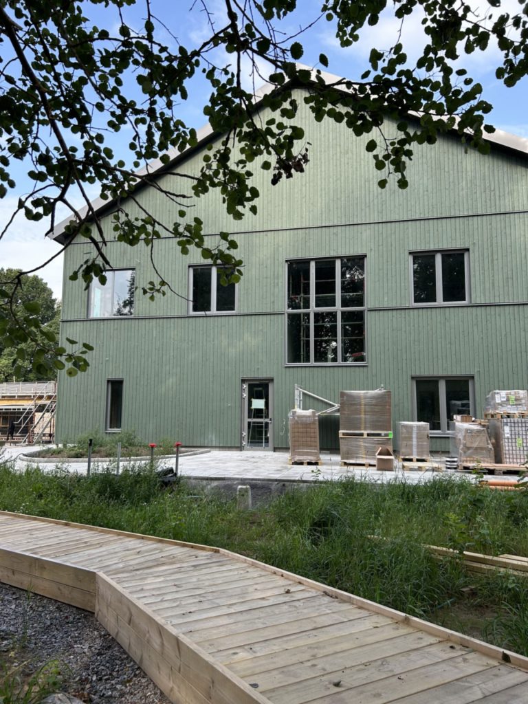 Grön husfasad bakom lövverk och träspång.