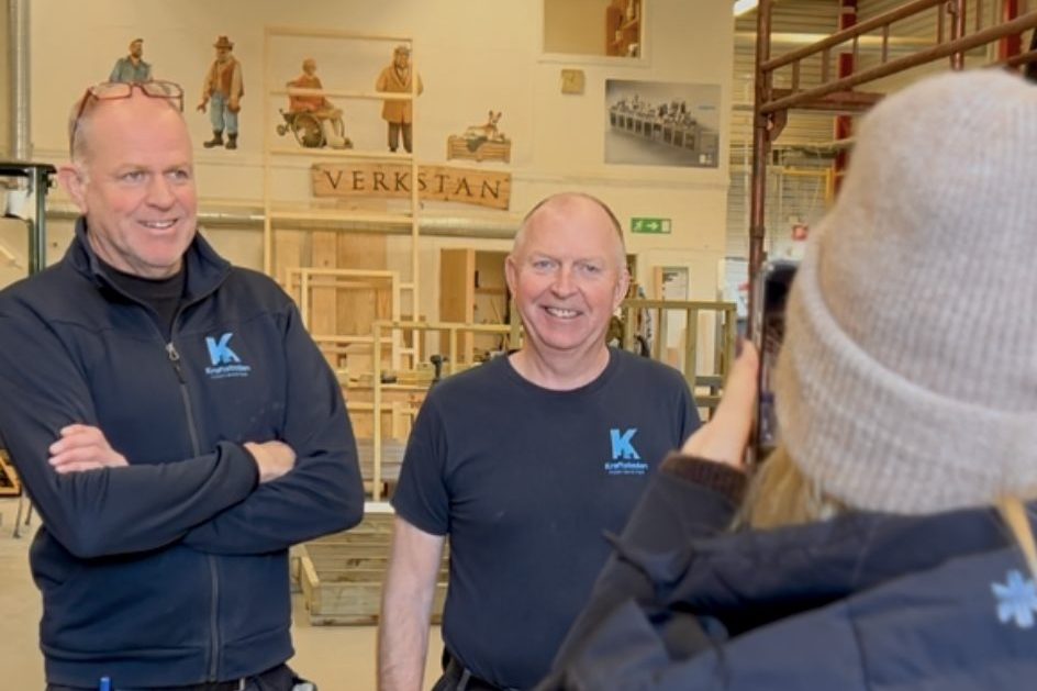 Frank och Mikael tittar mot kameran. I bakgrunden syns den stora snickarverkstaden.