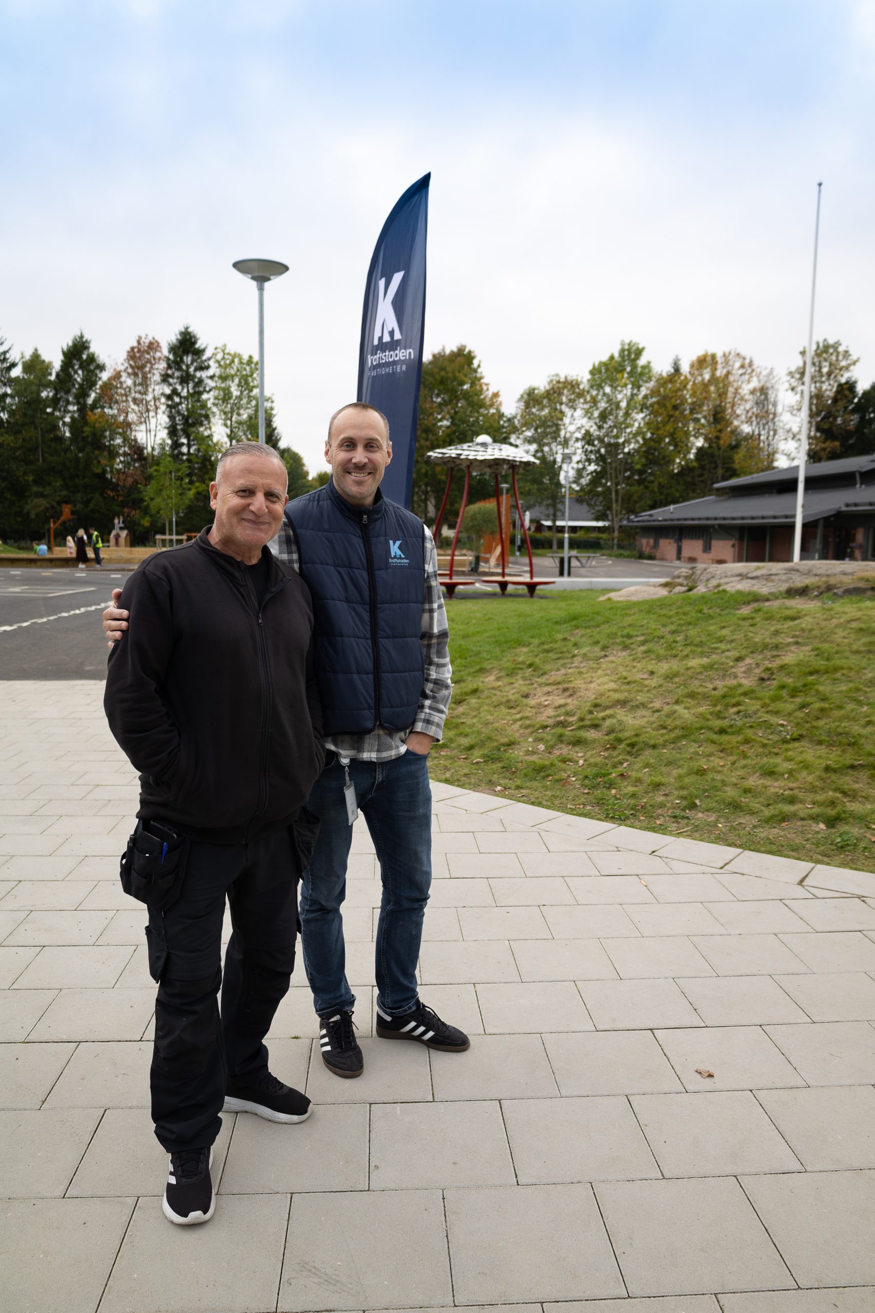 Två män på utegården som leende väntar på bandklippningen.